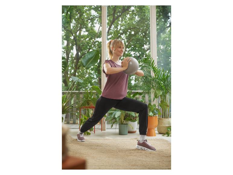 Femme en tenue de sport faisant une fente avec un ballon gris sur une terrasse.