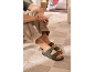 Sandales vertes pour hommes avec boucles, pantalon beige et t-shirt vert, assis sur un tapis.