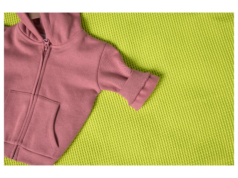 Sweat à capuche rose sur une couverture texturée vert citron.