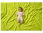 Bébé en grenouillère blanche allongé sur une couverture gaufrée verte.