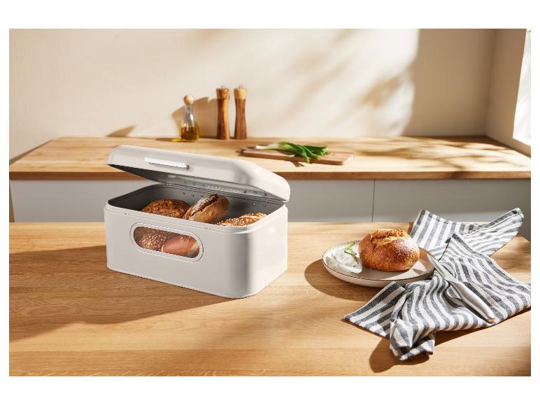 Une boîte à pain beige avec du pain sur une table en bois dans une cuisine.