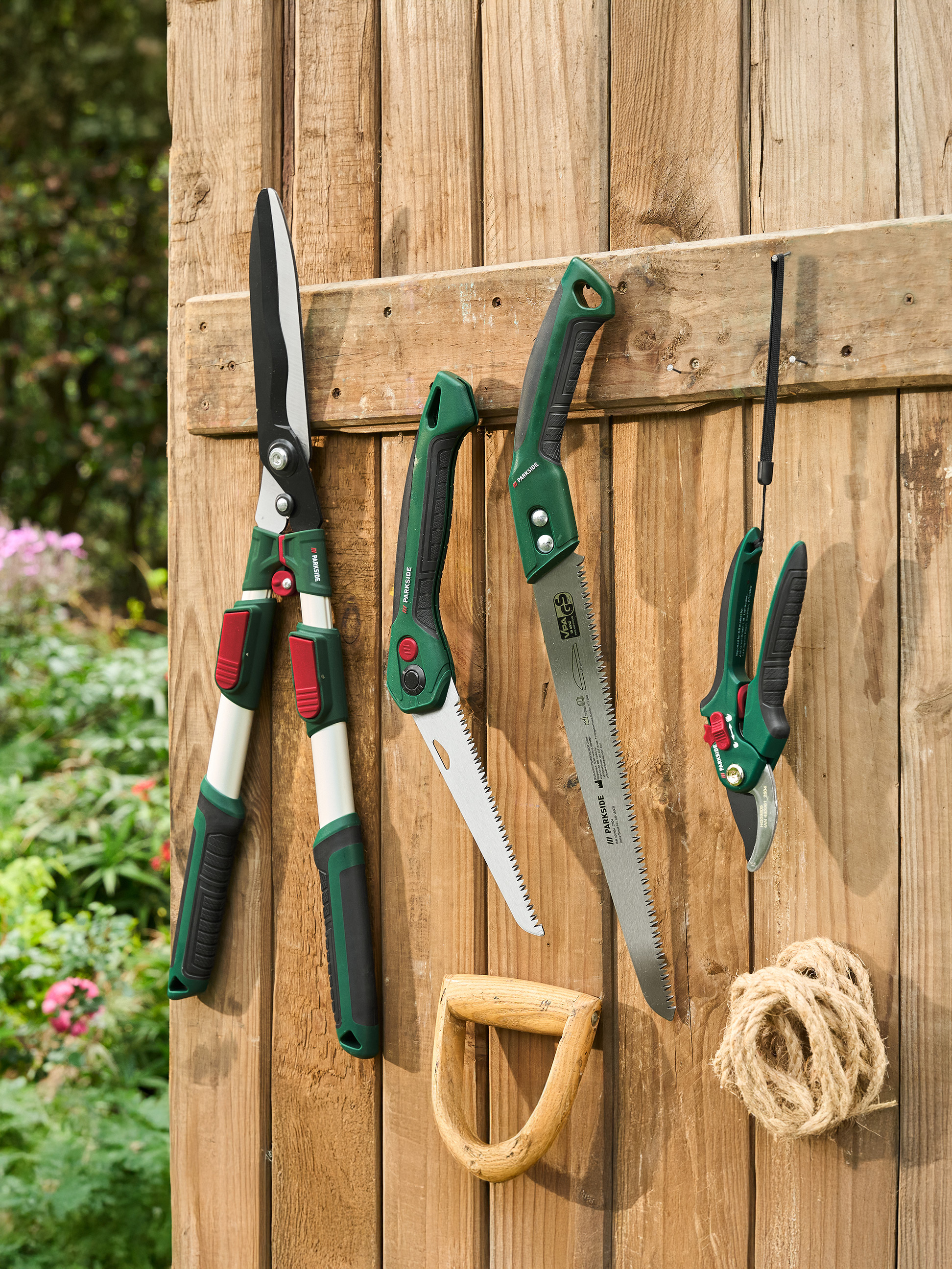 Sécateurs, scies et cisailles de jardin PARKSIDE suspendus à une clôture en bois.