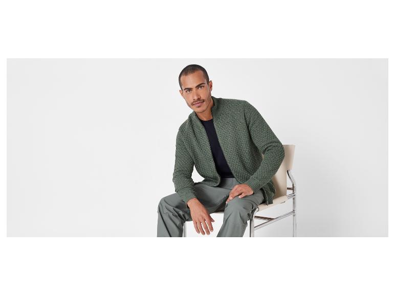 Un homme portant un pull vert et un pantalon assis sur une chaise.