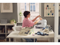 Femme cousant sur une machine à coudre, entourée d'accessoires de couture et de boîtes de rangement.
