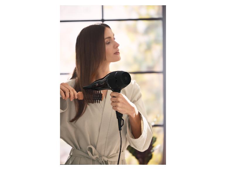 Femme se séchant les cheveux avec un sèche-cheveux et une brosse ronde.