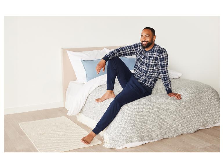 Un homme en pyjama à carreaux assis sur un lit avec un couvre-lit blanc.