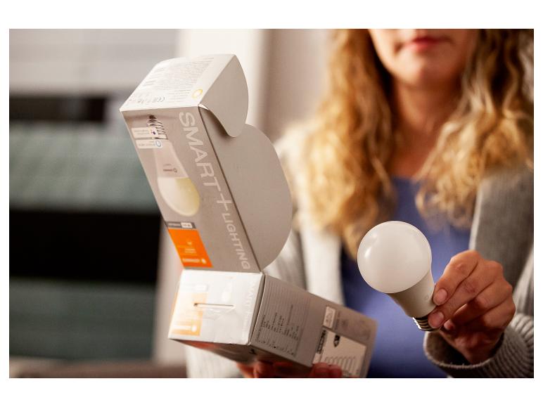 Femme tenant une ampoule intelligente et son emballage 'SMART+ LIGHTING'