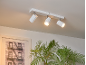 Spot de plafond blanc avec trois lampes réglables, éclairant une image encadrée et une plante.