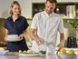 Un homme utilise un robot de cuisine Silvercrest tandis qu'une femme tient une pile d'assiettes.