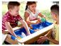 Enfants jouant avec une table à eau en bois avec des bacs bleus et des jouets.