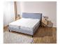 Un lit gris avec un protège-matelas blanc et un tapis blanc.