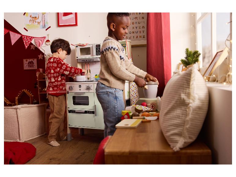 Deux enfants jouent avec une cuisine jouet et des aliments en bois.