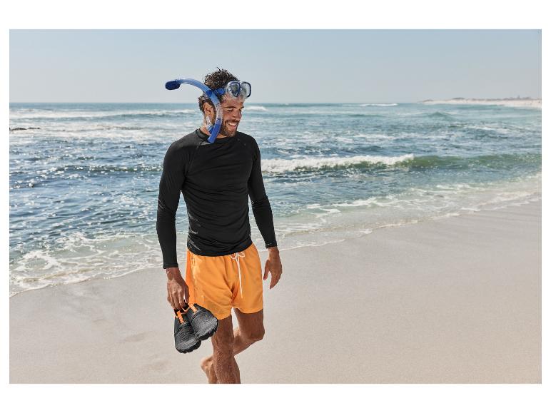 Homme en t-shirt noir, short orange, masque de plongée et chaussures aquatiques sur la plage.