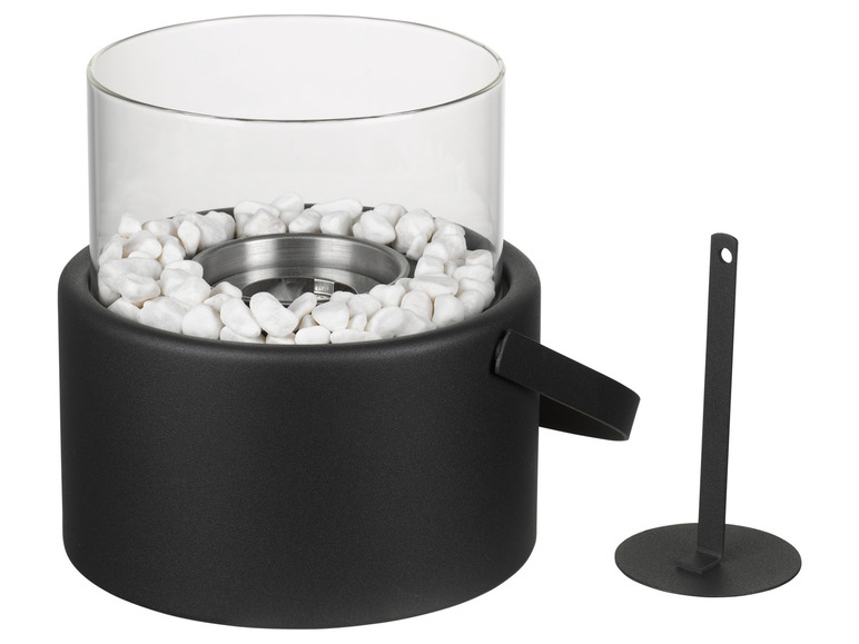 Un brasero noir avec un pare-vent en verre et des pierres blanches décoratives.