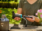 Une femme tient un pulvérisateur et une batterie Gardena.