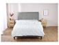 Une couette blanche avec un motif en losange sur un lit gris dans une chambre.