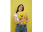 Femme souriante tenant un ours en peluche jaune sur fond jaune.