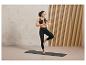 Une femme en brassière de sport et leggings noirs fait du yoga sur un tapis.