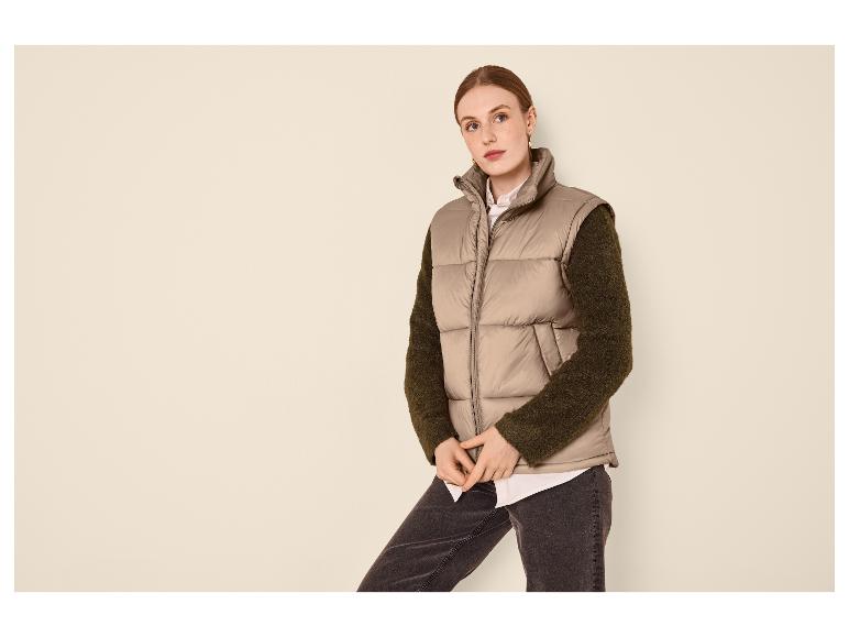 Femme en gilet matelassé beige, chemise blanche et jean foncé.