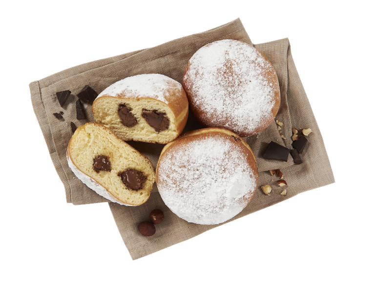Beignets fourrés au chocolat et saupoudrés de sucre glace, servis sur un tissu en lin avec des noisettes.