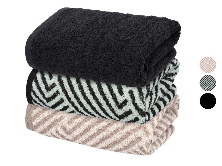 Pile de trois serviettes pliées : noire, vert clair avec motif noir et beige avec motif.