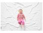 Un bébé en vêtements roses sur une couverture blanche.