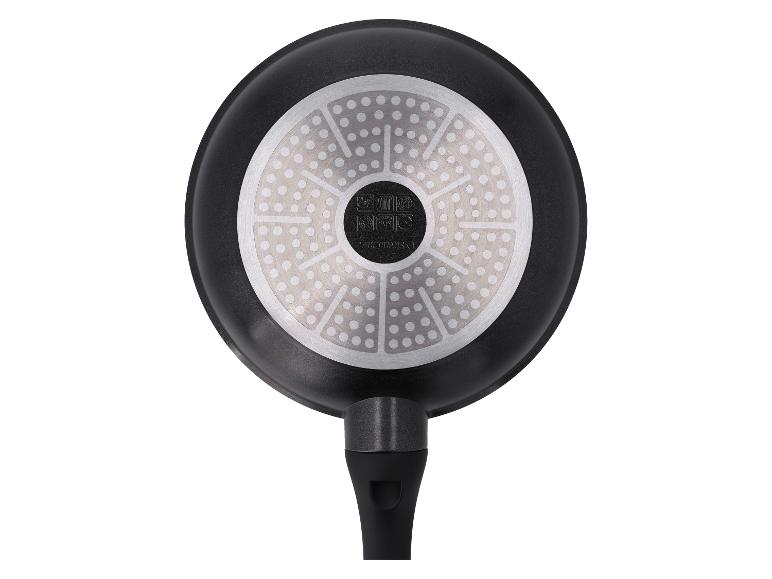 Dessous d'une poêle noire avec un fond métallique circulaire à motifs et une poignée noire.