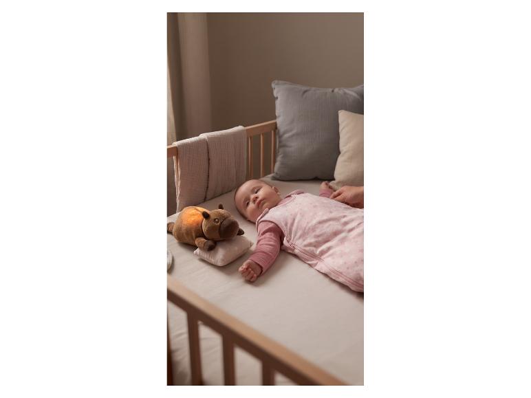 Bébé dormant dans un berceau en gigoteuse rose avec une peluche lumineuse.