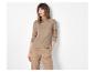 Femme en haut côtelé marron et pantalon marron posant contre un mur blanc.