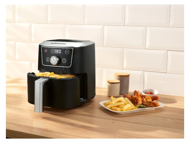 Friteuse à air noire avec frites et ailes de poulet sur un comptoir en bois.