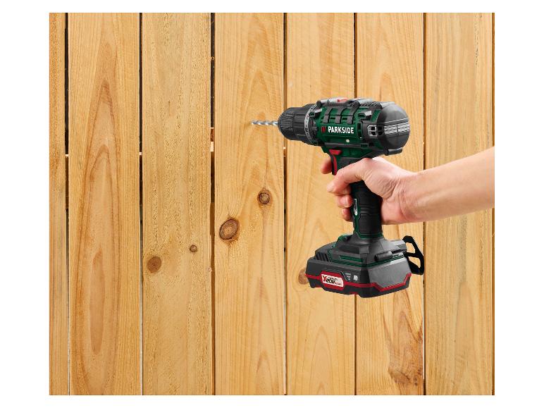 Une main tient une perceuse sans fil Parkside, perçant une clôture en bois.