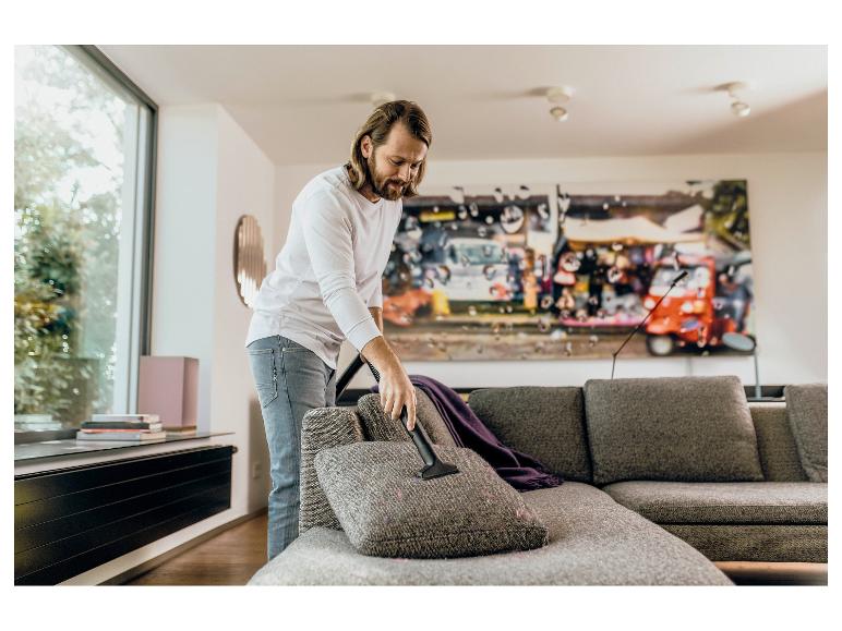 Homme passant l'aspirateur sur le canapé avec un aspirateur à main dans le salon.