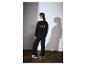 Femme en sweat-shirt noir à logo et pantalon noir, regardant à gauche.
