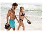 Couple en maillot de bain et claquettes marchant sur la plage, souriant.