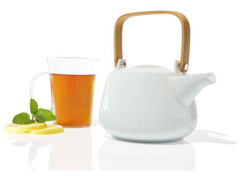 Une théière blanche avec une poignée en bois et un verre de thé au citron et à la menthe.