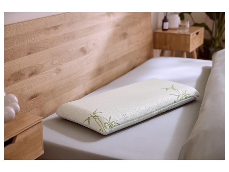 Oreiller en mousse à mémoire de forme blanc avec motif bambou vert sur un lit avec tête de lit en bois.