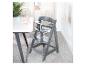 Chaise haute grise avec plateau à côté d'une table blanche avec bols et tasse.