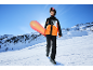 Jeune personne en veste et pantalon de ski avec snowboard sur une montagne enneigée.