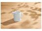 Pot à lait en céramique blanche sur une table en bois clair avec des taches de soleil et des ombres
