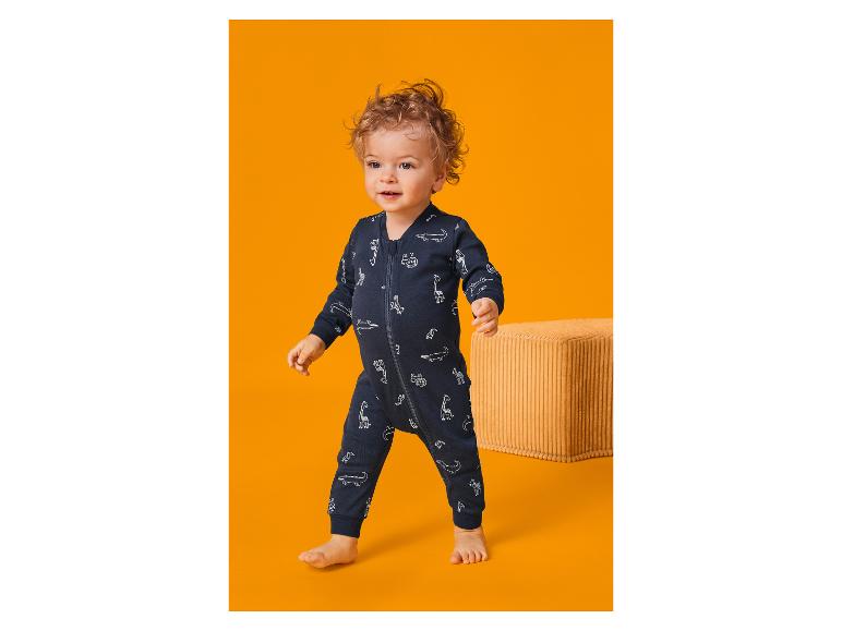 Bébé en barboteuse bleu marine à imprimé animal, marchant sur un fond orange.