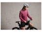 Une femme en veste rose et casque de vélo sur un vélo noir