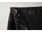 Gros plan sur la taille d'un pantalon noir avec fermeture éclair, bouton et agrafes.