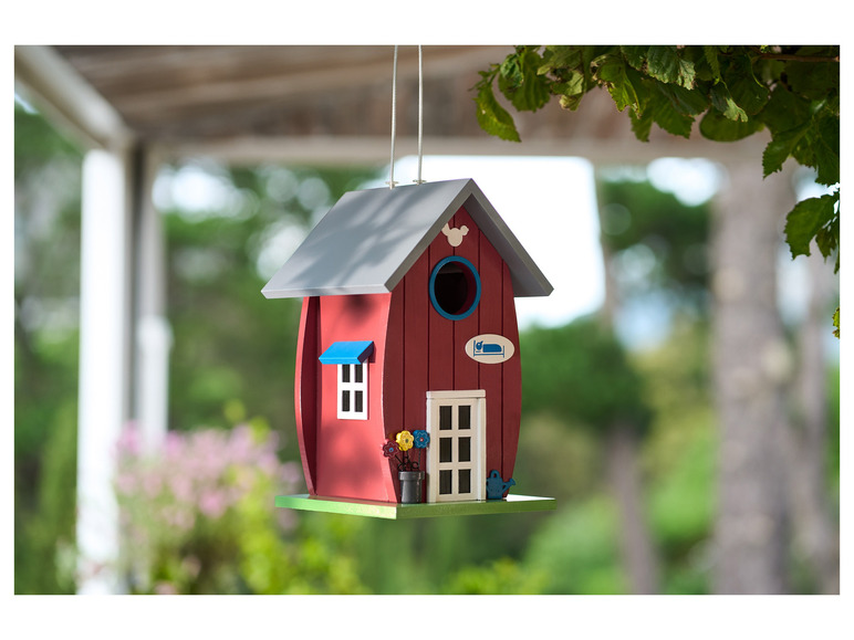 Une maison à oiseaux en bois rouge avec un toit bleu et des fleurs.