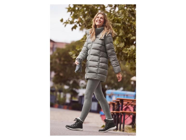 Une femme en veste d'hiver grise, leggings et bottes noires marchant dans la rue.