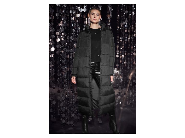 Femme en longue doudoune noire, pantalon en cuir noir et bottes devant un fond scintillant.