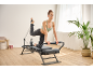 Femme pratiquant le pilates sur un appareil reformer dans une pièce lumineuse.