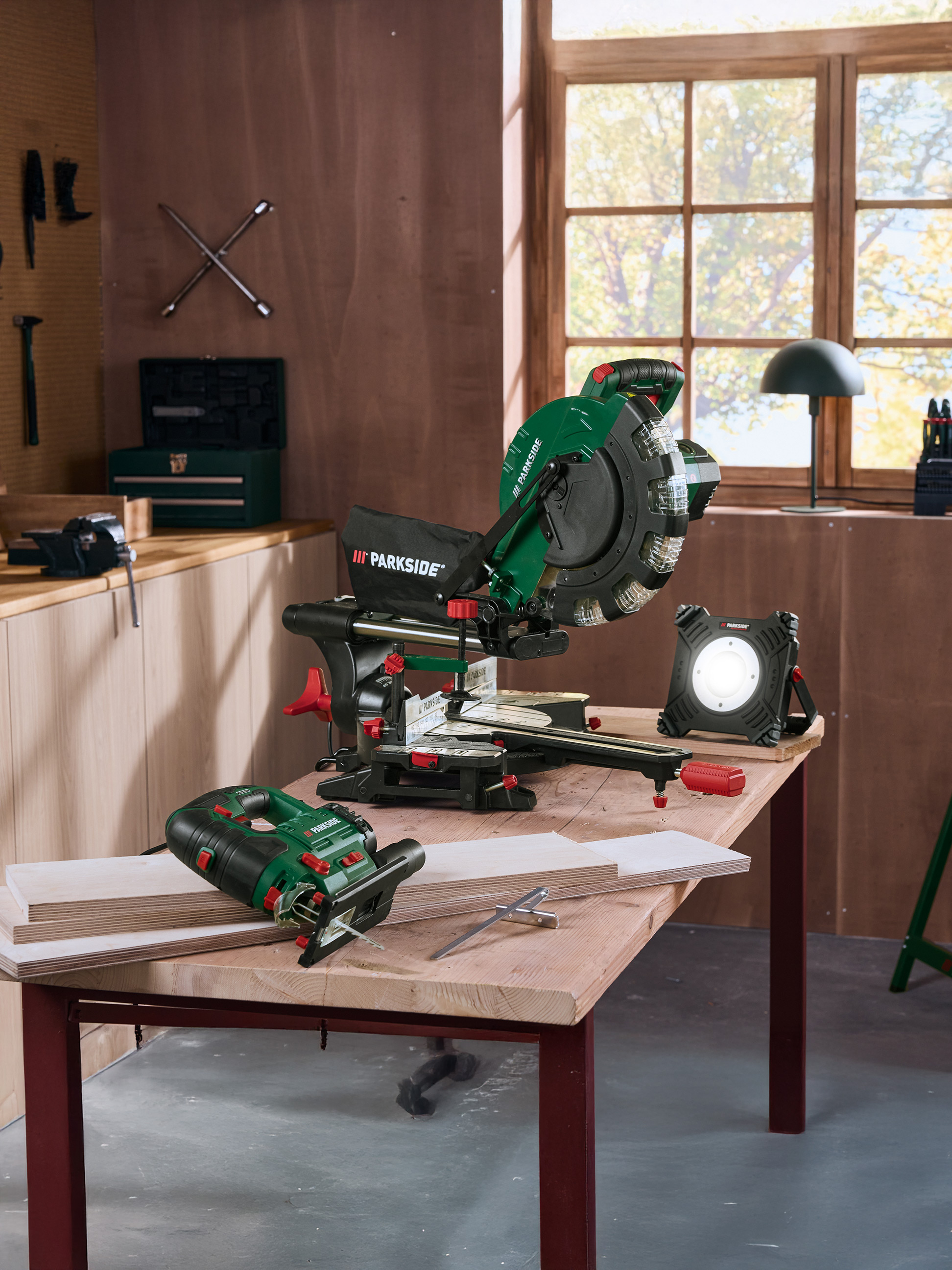 Outils Parkside : scie à onglet, scie sauteuse et lampe de travail sur une table en bois dans un atelier.