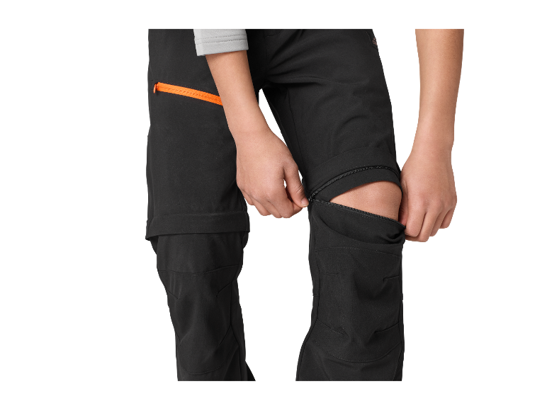 Enfant ajustant un pantalon softshell avec fermetures éclair aux genoux.