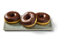 Trois beignets glacés au chocolat sur un plateau rectangulaire.