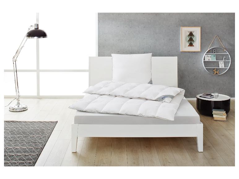 Lit blanc avec couette et oreiller, lampe de lecture et table d'appoint dans une chambre moderne.